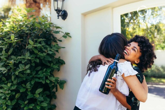 African woman greeting and embracing female friend for having a new house. Smiling young woman with wine bottle congratulating her friend. Housewarming with friends.