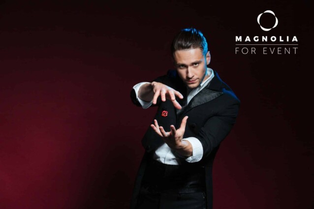 Concentrated young man magician conjuring tricks with red dice  over dark background