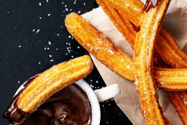 Churros with sugar dipped in chocolate sauce on a black background. Churro sticks. Fried dough pastry, top view